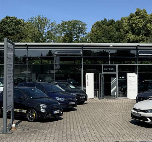 Fahrzeugausstellung mit mehreren Autos vor Glasfassade bei Sonnenschein