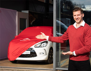 Mitarbeiter präsentiert weißes Fahrzeug unter rotem Tuch vor dem Arndt Tuning Berlin Showroom – Symbolbild für Fahrzeugverkauf