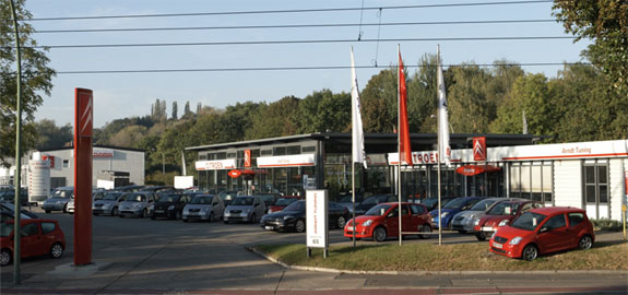 Firmengebäude Arndt Tuning Berlin – Autohaus mit Fahrzeugausstellung, Fahnen und roten Säulen bei Sonnenschein