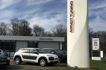 Hofeinfahrt Arndt Tuning Berlin – weißes Citroën Fahrzeug vor Firmengebäude und Pylon mit Logo bei Sonnenschein